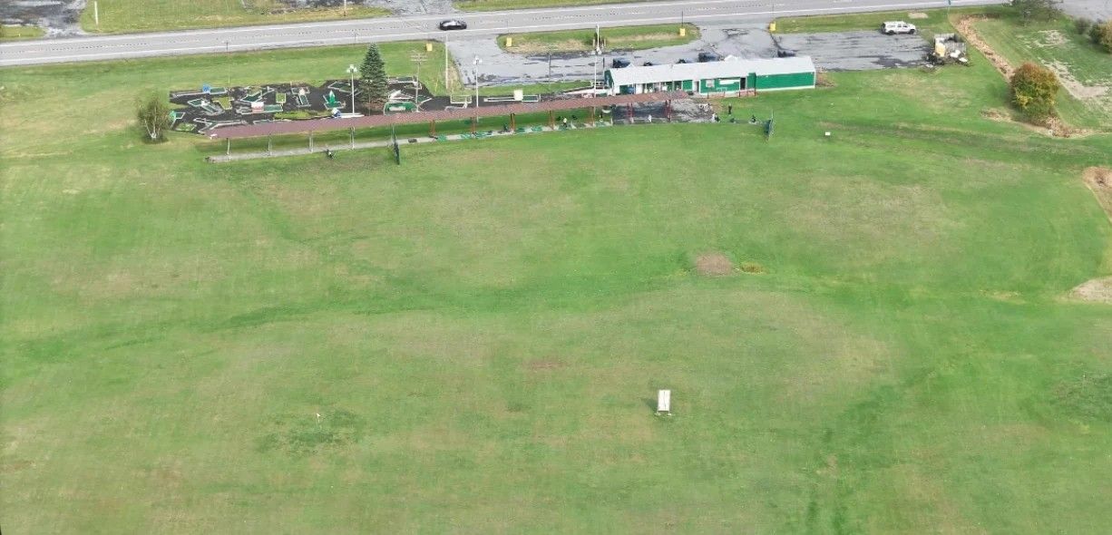 Aerial view of CNY Golf Shop & Range: the green and white shop and the covered tee line beside Route 11, with the wide open practice field in front.