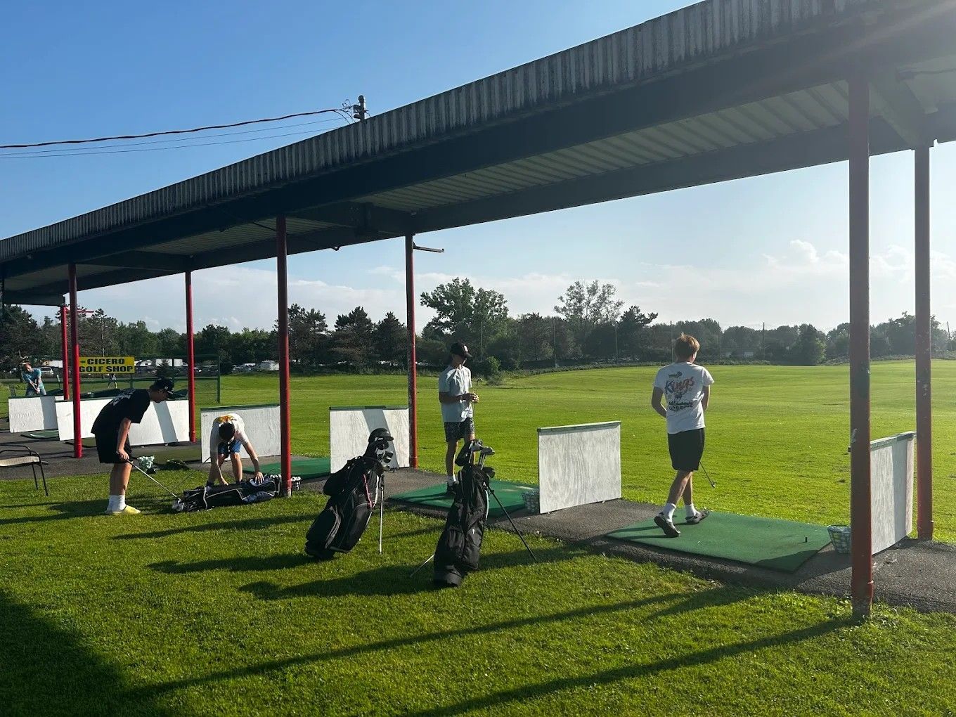 Golfers practicing under the covered tee line at CNY Golf Shop & Range on a sunny day, with the open range behind them.