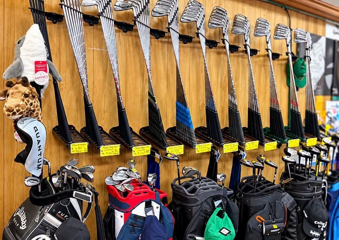 A wall of used iron sets on racks inside the shop, each with a yellow price tag, above a row of golf bags.